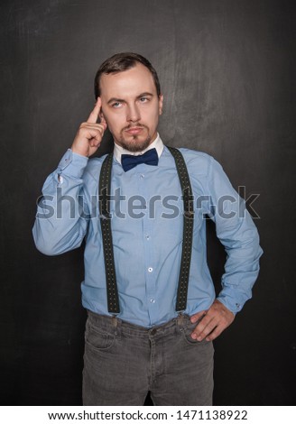 Thoughtful young businessman or teacher looking up on blackboard background