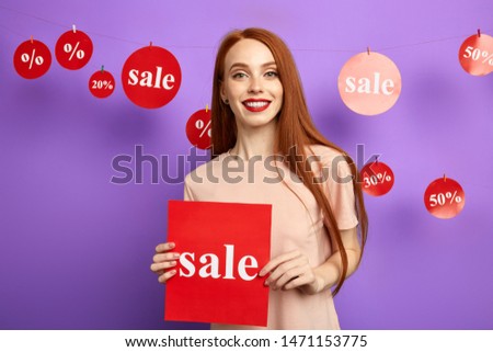 attractive young woman holding a board , showing sale, inviting people to a shop. isolated blue background, studio shot.