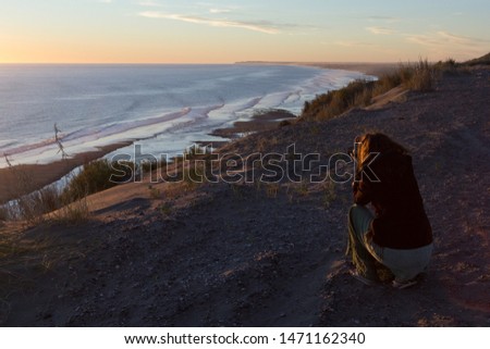 Woman taking a picture of the sea at sunset from a cliff