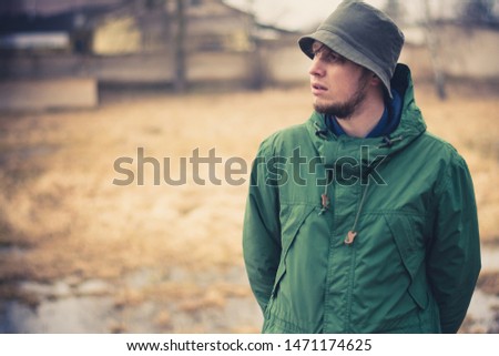 a young guy in a swampy area stares away. Casual wear, khaki pants, green jacket, green panama. In the background a swamp and flooded houses Royalty-Free Stock Photo #1471174625
