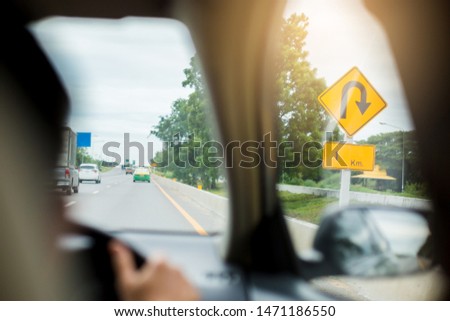 Blurry traffic signs of U-Turn and 1 km on yellow background with the highway  traffic in Thailand, Image of U-Turn arrow with 1 km, View from inside car with driver is driving. Drive safety concept.