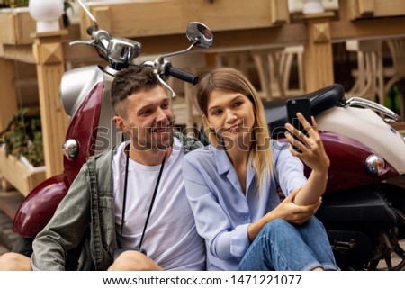 Happy couple on scooter making selfie photo on smartphone outdoors. People Travel On Weekend. High Resolution.
