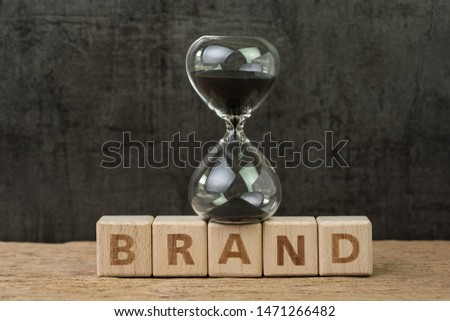 Brand communication for product and service advertising, Hourglass or sandglass on wooden cube block with alphabet building the word Brand on wood table, dark black background.