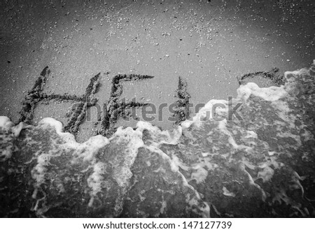 HELP inscription on the beach sand washed by sea wave. Black and white photo. Vignette.