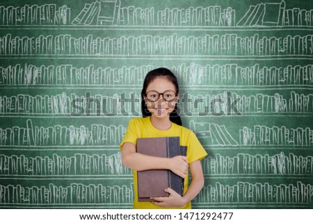 Female elementary school student smiling at the camera while holding books in the library with drawn bookcase background