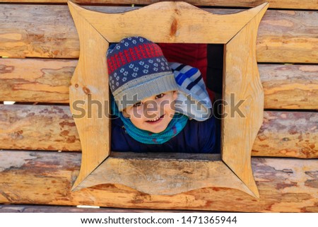 smiling five-year-old boy boy looks out the window of the house. children's wooden house on the Playground outdoors