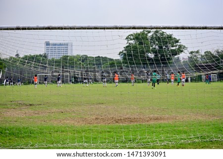 Boys are playing soccer in soccer field, Picture is captured behind soccer goal.