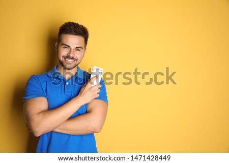 Happy young man with air conditioner remote control on yellow background. Space for text