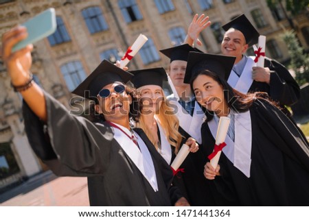 Remembering the moment. Happy graduates holding their diplomas standing together near their university and taking a selfie.