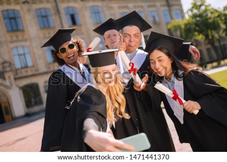 Photo for memory. Beautiful girl taking pictures with her groupmates after graduation in the university yard.