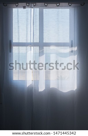 Transparent curtain with the shadow of the silhouette of the window and sunlight. View through the curtains to the sea and beach.  Concept interior.