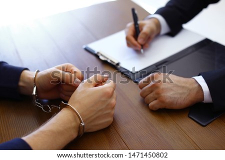 Police officer interrogating criminal in handcuffs at desk indoors Royalty-Free Stock Photo #1471450802