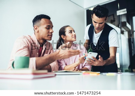 Millennial hipster guys cooperating et desktop during learning process and discussing information from content website, diverse male and female student brainstorming on university course work