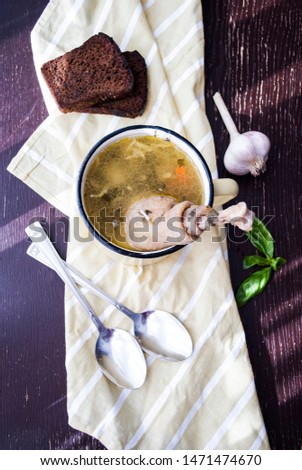 
Rustic style zama soup with noodles and homemade chicken. Moldavian, traditional dish. Bouillon in an old jug on a wooden table with a towel. Two spoons, garlic, basil, two slices of fried bread
