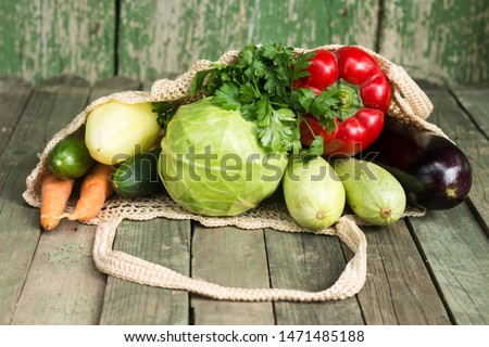 Vegetables in a string bag on a wooden background. Pepper, cabbage,parsley,cucumber,carrot, eggplant,chili, marrow