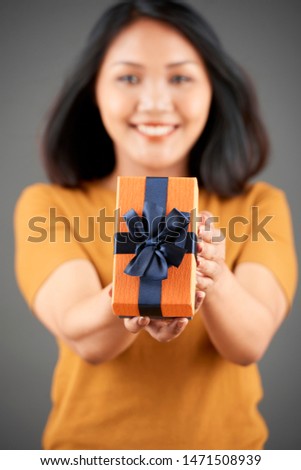 Portrait of Asian woman holding present with ribbon giving to you and smiling isolated on grey background focus on foreground