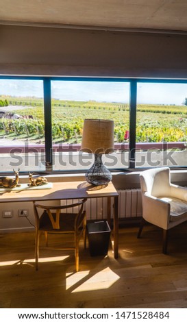 Beautiful view of green vineyards and clear blue sky, from hotel window. View of winery landscape from inside hotel room with desk, lamp, chair, in romantic retreat resort. Shot in Mendoza, Argentina