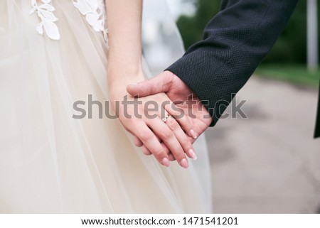 Bride, wearing ivory wedding dress, and groom, wearing black suit, holding hands. Close-up picture of hands.  Wedding couple walikng with hands together. Romantic stroll in the park. 