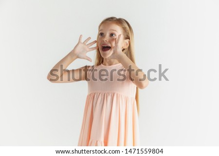 Stylish little smiling girl posing in dress isolated on white studio background. Caucasian blonde female model. Human emotions, facial expression, childhood. Calling, astonished, wondered.