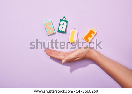 cropped view of hand of woman near colorful paper bags with sale lettering on violet