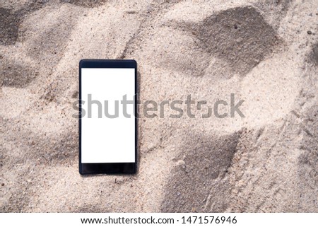 stock photo phone on the beach, black smartphone show white screen lying on white sand in day light, blank for text ads and graphic design. Summer, Travel and Technology concept with copy space