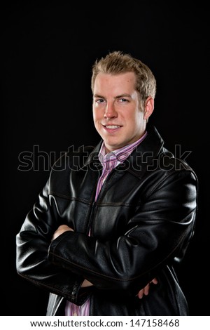 Portrait of a young male model wearing a black leather jacket and colorful striped shirt.  He's smiling with his arms crossed and is shot on a black background.