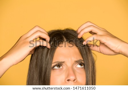 Beautiful young woman with itchy scalp on yellow background