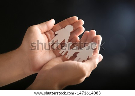 Man holding paper silhouette of family in hands on dark background, closeup