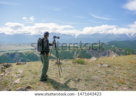 Travel photographer man taking nature photo or video of mountain landscape. A man photographer is setting up a camera standing on a tripod. 