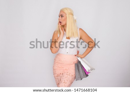 Young blonde woman holding shopping bags in hands, posing on a white background in the studio