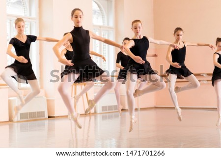 Medium group of teenage girls practicing ballet moves in a large dancing studio. Performing Pas de Chat jump Royalty-Free Stock Photo #1471701266