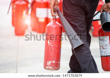 Closeup of fireman lower body prepare to fire drill by holding portable fire extinguish and water hose. Security insurance protection and fire fighter concept. Many red dry chemical tank background.