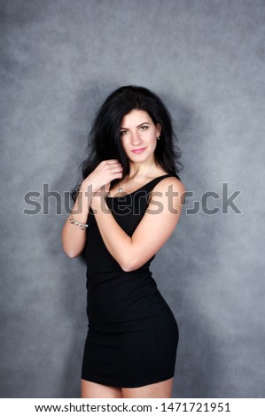 Portrait of a beautiful brunette girl with thick hair and in a short black dress