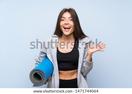 Young sport girl with mat over isolated blue background with shocked facial expression