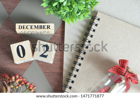 December 2. Date of December month. Number Cube with a flower, Rose bottle and notebook on Diamond wood table for the background.