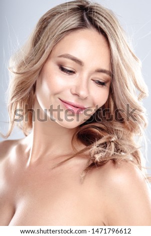 Blonde young woman with healthy curly hair and natural make up . Beautiful model girl with wavy hairstyle. Care and beauty