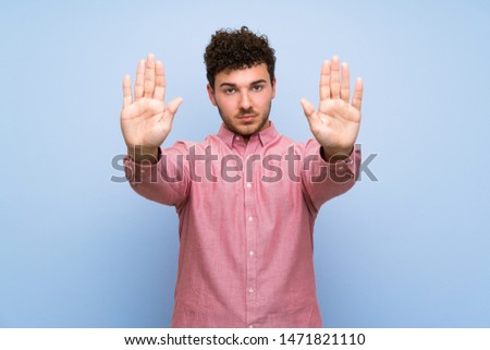 Man with curly hair over isolated blue wall making stop gesture and disappointed