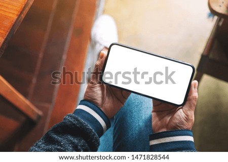 Top view mockup image of hands holding black mobile phone with blank desktop screen