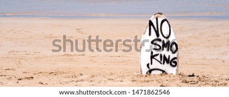 "No Smoking" warning sign on white surfboard at the beach in summer, concept of sea environmantal protection design, copy space, lifestyle.