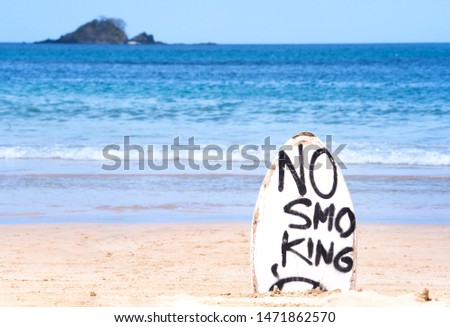 "No Smoking" warning sign on white surfboard at the beach in summer, concept of sea environmantal protection design, copy space, lifestyle.