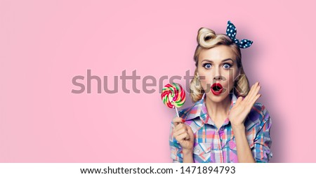 Excited surprised woman with lollipop. Girl pin up with open mouth. Blond model at retro fashion and vintage concept. Pink color studio background. Copy space for some advertise slogan, sign or text. 