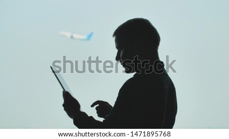 Silhouette of young men using tablet pc on the background of an airplane taking off.