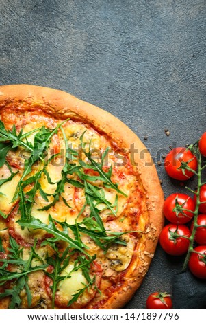 Traditional Italian pizza with arugula and tomatoes on a dark background top view copy space.