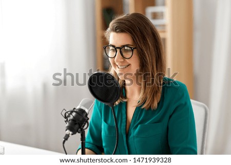 technology, mass media and people concept - woman in glasses with microphone talking and recording podcast at studio
