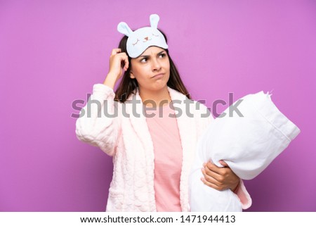 Young woman in pajamas and dressing gown over isolated purple background having doubts and with confuse face expression