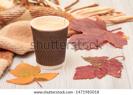 Cup of coffee, checkered wool plaid and dry leaves on gray wooden boards. An autumn still llife.