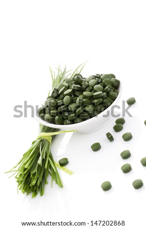 Wheatgrass blades and green spirulina pills isolated on white background. Healthy green eating. Vegan food supplement.