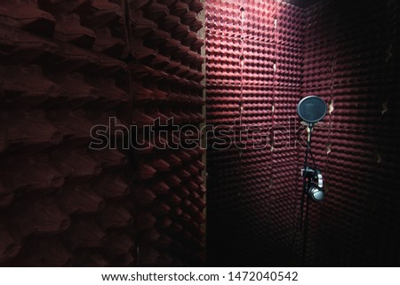 Interior of recording studio with microphone on a support stand and headphones. Red soundproof walls. Egg carton.