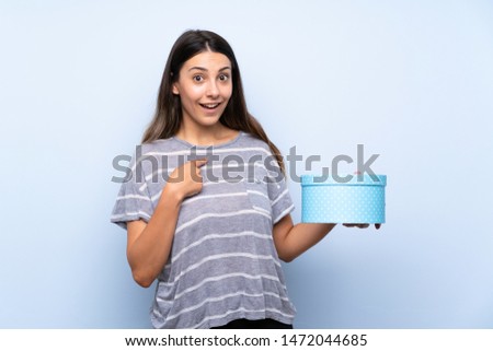 Young brunette woman over isolated blue background holding gift box