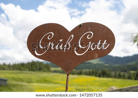 rusty welcome sign with german letters in the shape of a heart in an alpine pasture